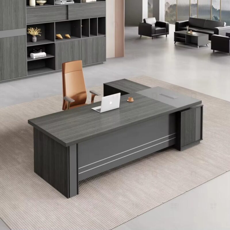 Modern L-shaped executive desk in a sleek gray wood grain finish, featuring a thick floating tabletop design supported by a dark charcoal sub-frame, a matching integrated side return storage cabinet, and a metallic-trimmed gray modesty panel.