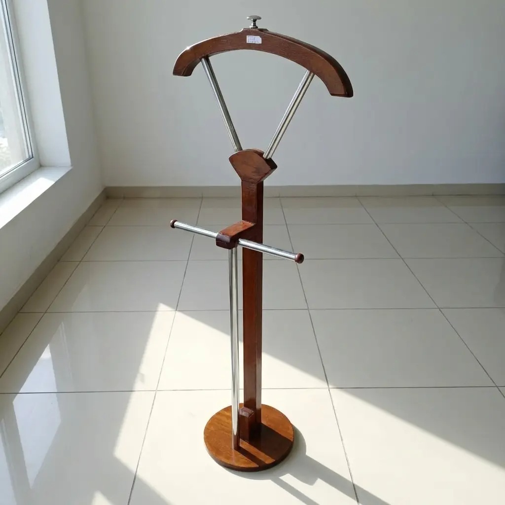 Modern freestanding wooden valet stand with a curved suit hanger, metal trouser bar, and a stable circular base in a minimalist white-tiled room.