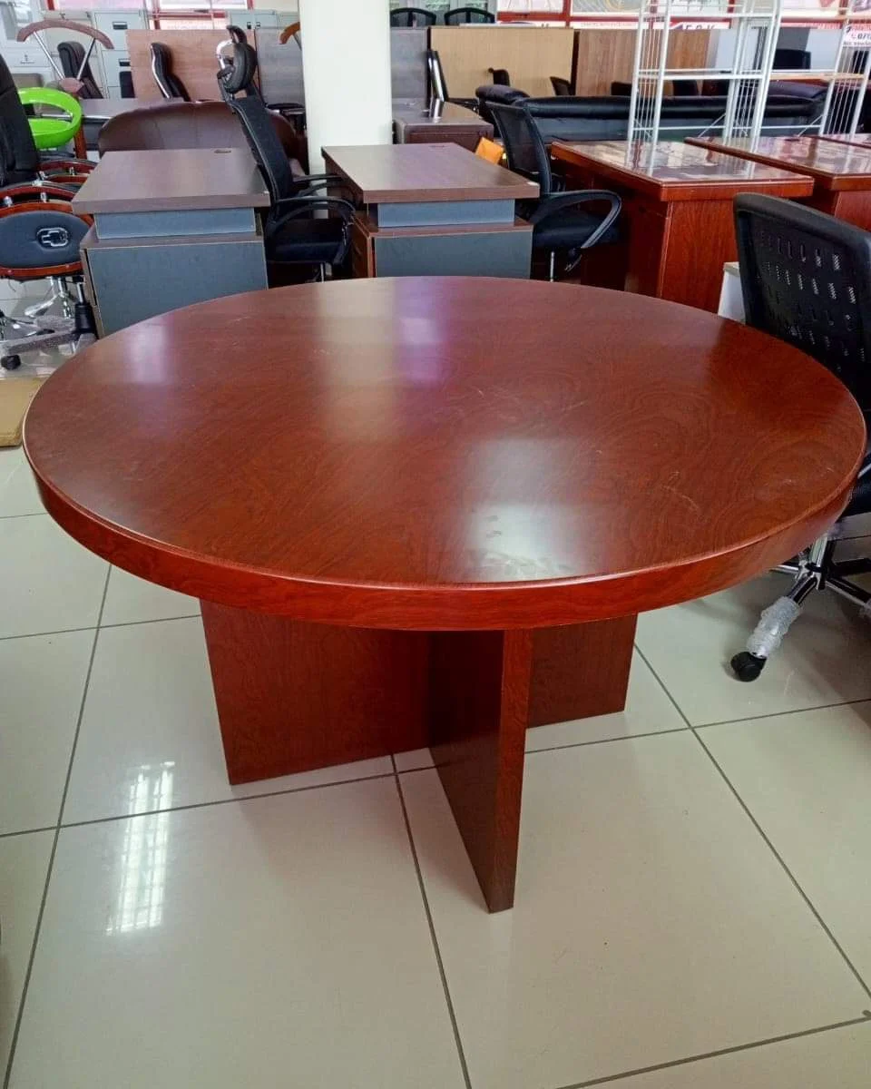 Round conference table in a rich cherry wood veneer finish, featuring a thick, circular tabletop with a classic bevelled edge detail, supported by a central, intersecting X-shaped wooden pedestal base.