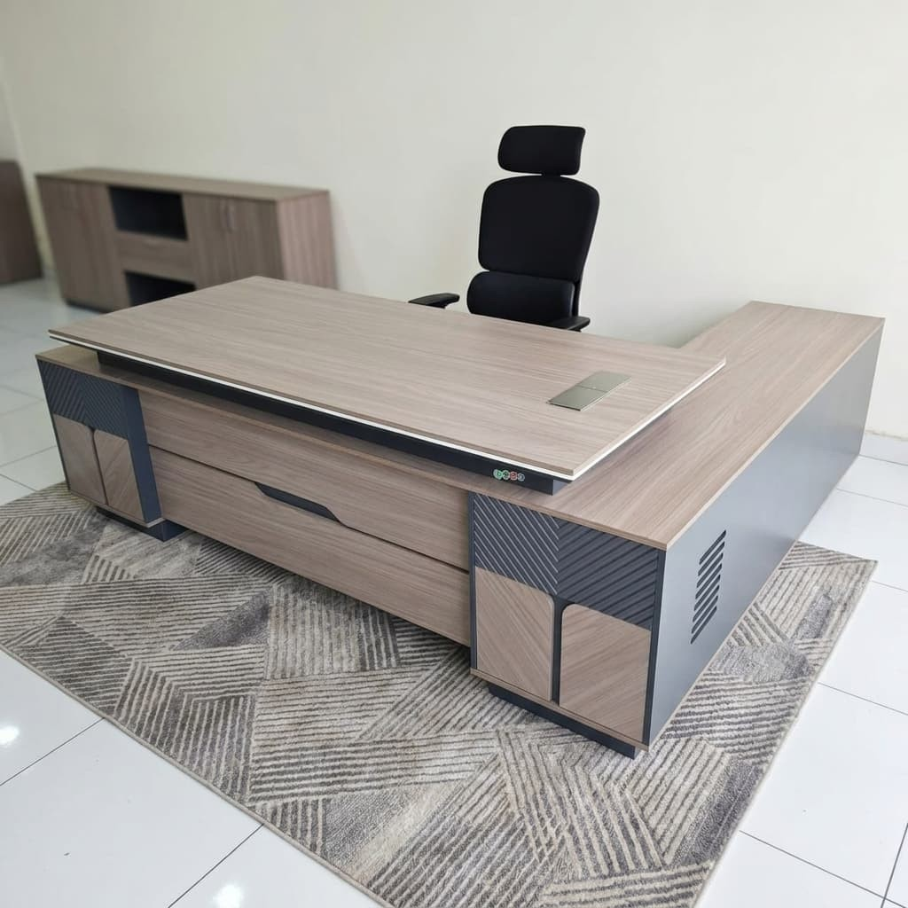 2.4m managerial executive desk in an L-shaped configuration featuring a light oak wood grain melamine floating tabletop with an embedded silver rectangular cable flip-box, an integrated charcoal grey side return credenza, and a textured front modesty panel accented with fluted dark grey panels and wood-toned cabinet facades.