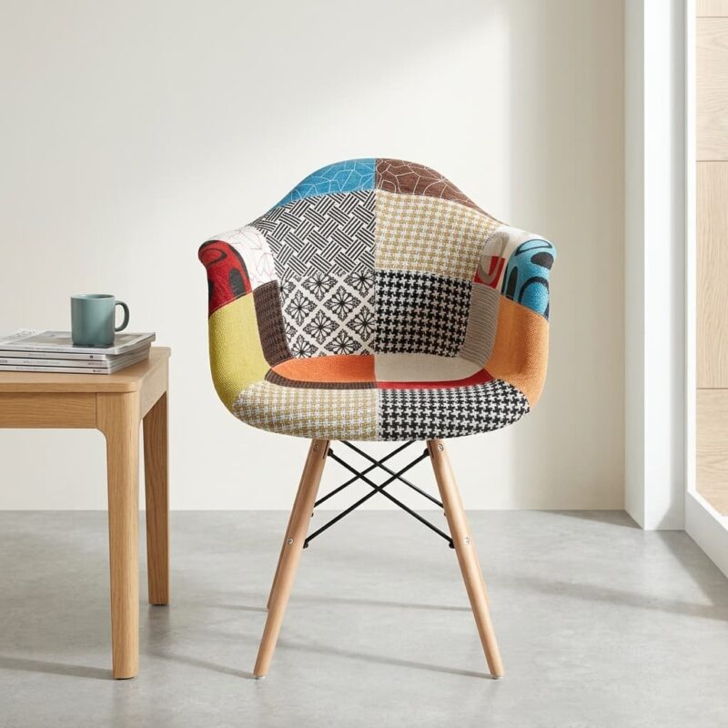 Eames armrest patchwork chair featuring a molded shell seat fully upholstered in a vibrant multi-patterned fabric collage including houndstooth, stripes, and geometric prints, supported by a light wood dowel base with black metal Eiffel-style wire bracing.