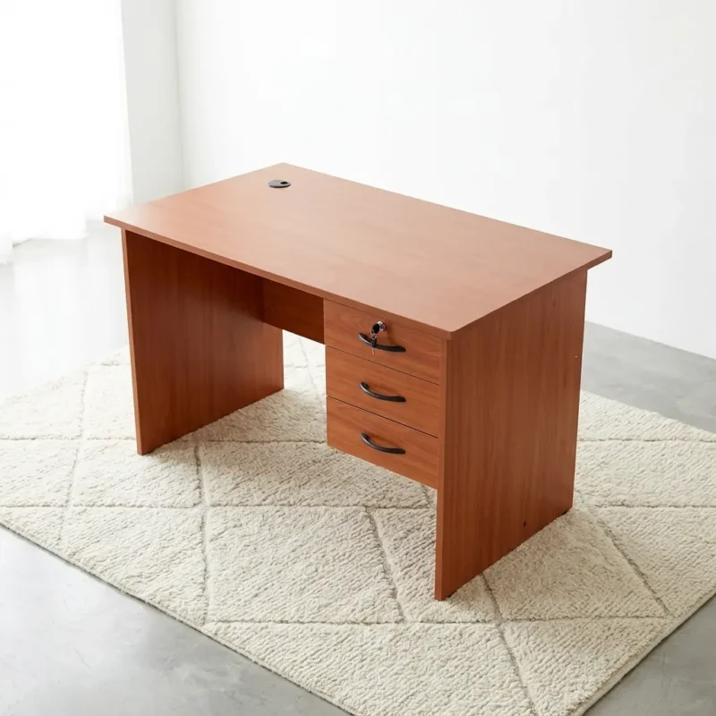 Compact 1.0m home office desk in a cherry wood finish, featuring an open right-hand three-drawer pedestal with curved black handles, a key-lock top drawer, a rectangular writing surface with a black cable grommet, and an integrated modesty panel.