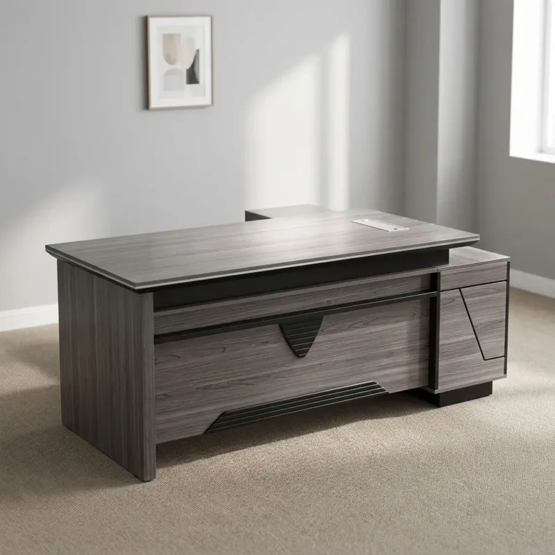 L-shaped 1600mm Office Table featuring a contemporary grey wood-grain laminate finish, an integrated desktop flip-top cable management box, a front modesty panel with geometric black accent detailing, a side return extension unit with integrated cabinet storage, and solid panel-style engineered wood base supports.